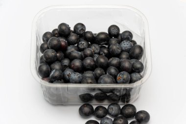 Beyaz arka planda şeffaf plastik bir kapta yabanmersini var.