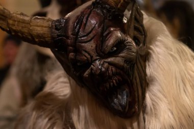 Krampus 'un devasa boynuzları ve hafif kürklü görüntüsü akşam kalabalığına karşı