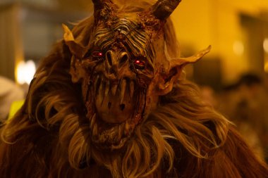 Parlayan kırmızı gözlü Krampus maskesi akşam vakti sıcak sokak lambalarıyla aydınlatılır.