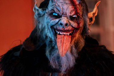 Krampus 'un dili çıkmış, parlayan gözleri ve maskede görünür makyaj ayrıntıları olan yakın çekimi.