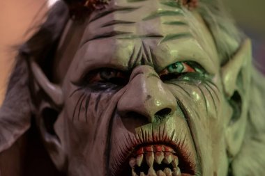Krampus maskesi, buruşuk yüzlü, çıplak dişli ve sert yan ışıklandırmalı.