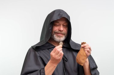 Yaşlı, sakallı bir keşiş, beyaz arka planda bir para ve bir çanta tutuyor.