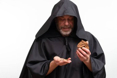 Siyah cüppeli keşiş beyaz arka planda keseden bozuk para döküyor.