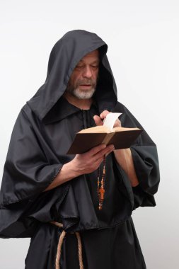 Erkek keşiş elinde tespih, siyah bornoz ile kitap okuyor.
