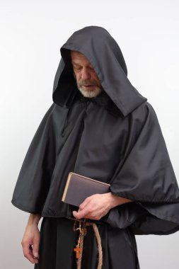 Erkek keşiş elinde kitap ve siyah bornoz ile tespih tutuyor.
