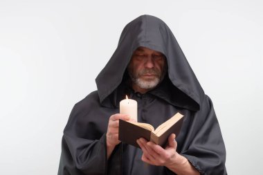 Kapüşonlu sakallı keşiş elinde mum tutuyor ve kitap okuyor.
