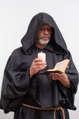 Sakallı keşiş mum ışığında metin okuyor.