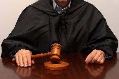 Siyah cüppeli yargıç duruşma sırasında tahta tokmağı mahkeme masasında tutuyor.