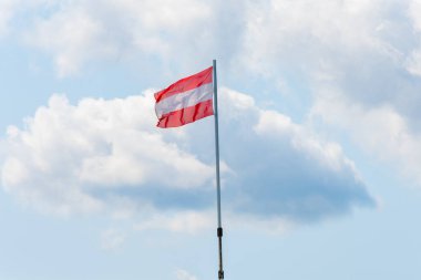 Kırmızı beyaz Avusturya bayrağı, bulutlu mavi gökyüzüne karşı rüzgarda dalgalanıyor.