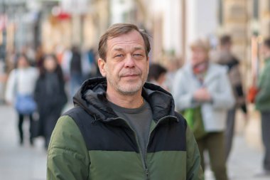 55 yaşındaki bir adam Avrupa şehir caddesinde yayaların arasında duruyor..