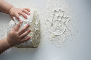 Hamur yoğuran küçük eller. Küçük çocuk mangırı desteklemek için hazırlıyor. Çocuk elleri, biraz un, buğday hamuru ve siyah masanın üzerinde merdane. Yemek pişirme konsepti.