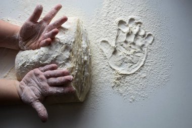 Hamur yoğuran küçük eller. Küçük çocuk mangırı desteklemek için hazırlıyor. Çocuk elleri, biraz un, buğday hamuru ve siyah masanın üzerinde merdane. Yemek pişirme konsepti.