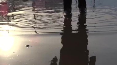 Lastik çizmeli bir çocuk su birikintisinde yürüyor. Bahar çamuru.