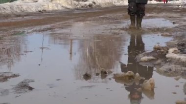 Lastik çizmeli bir çocuk su birikintisinde yürüyor. Bahar çamuru.