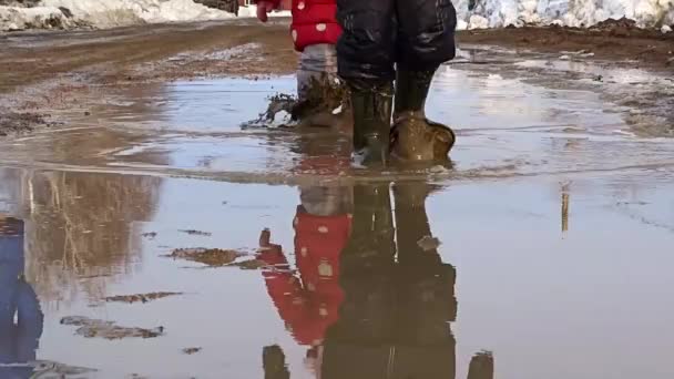 Un chico con botas de goma atraviesa un charco. Aguanieve de primavera. — Vídeo de stock
