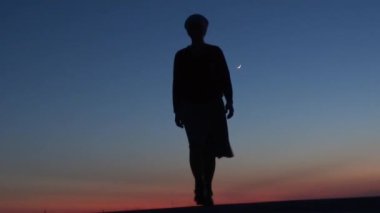 Gün batımında kız kıyıda duruyor ve uzaklara bakıyor, bir mucize bekliyor..