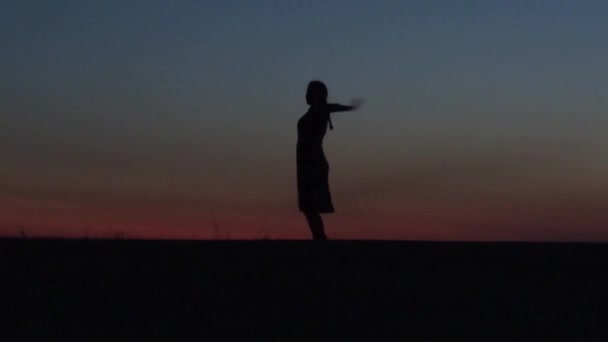 Ragazza in un abito fluente vortici contro il cielo del tramonto. silhouette di una giovane donna attraente. — Video Stock