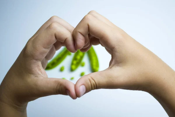 Erwt peulen liggen op een witte achtergrond, de kinderen handen in de vorm van een hart, Ik hou van groene erwten. — Stockfoto