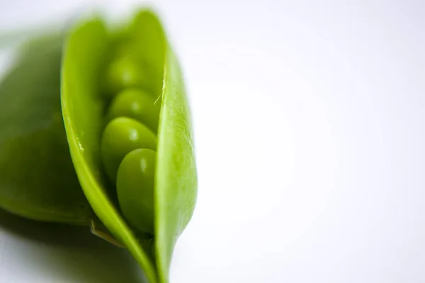 Frische grüne Erbsenschoten mit Laub auf weißem Hintergrund. Eine Schote ist offen, Erbsen sind sichtbar. — Stockfoto