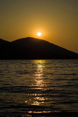 Dağın arkasında büyük bir gölün üzerinde akşam batımı. Dağların arasındaki gölde gün batımının romantik görüntüsü.