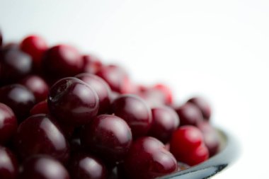 Beyaz arka plandaki kirazlar bir tabak içinde yatıyor. Makalen için kirazın yakın plan çekimi..