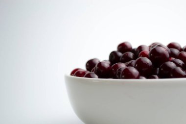 Beyaz arka planda beyaz bardakta koyu kırmızı kiraz.