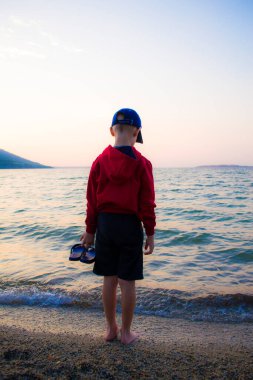 Gölün kıyısında yürümek için şapkalı bir çocuk, tecritten gelen çocukların psikolojik dinlenmesi, doğa iyileştirir..