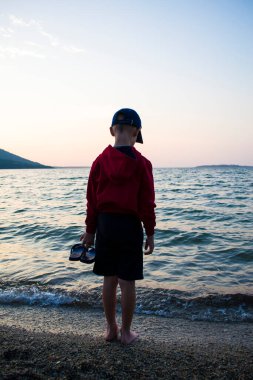 Gölün kıyısında yürümek için şapkalı bir çocuk, tecritten gelen çocukların psikolojik dinlenmesi, doğa iyileştirir..