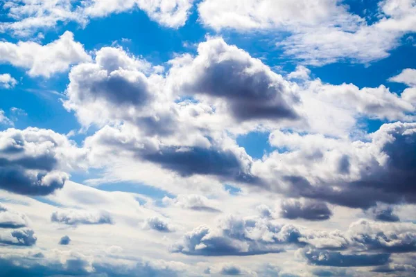 Ein blauer Himmel mit dramatischen Kumulonimbuswolken, umrahmt von silbrigem Kumulus und Cirruswolken, die über den Himmel verstreut sind. Gradienten blau. Hintergrundbild. Horizontales Foto. — Stockfoto