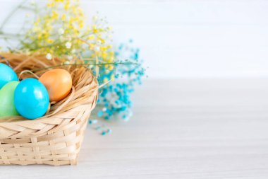 Çok renkli Paskalya yumurtaları beyaz ahşap bir masanın üzerinde duran sepetin içinde yatıyor.