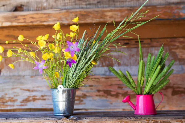 Fresh herbs and wildflowers in a small bucket and watering can on the old wooden background. Summer fresh concept.