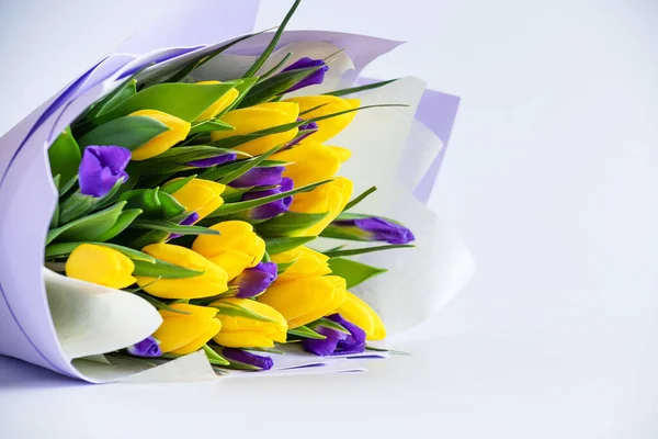Bellissimo bouquet di tulipani gialli e iris blu su sfondo chiaro. Sfondo floreale, biglietto primavera con fiori gialli e blu, spazio copia. Foto Stock Royalty Free