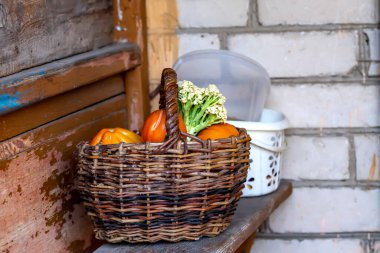 Üzerinde kırmızı domates ve karnabahar olan ahşap bir sepet eski bir ahşap bankta duruyor. Hasat..