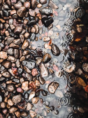 Kayalar, taşlar ya da çakıl taşları suyun üstünde, yağmur damlaları yüzeye vuruyor