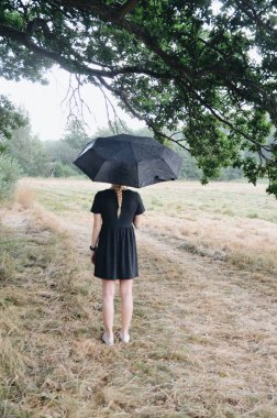Arkasından şemsiye tutan genç bir kadının fotoğrafı.