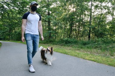 Maskeli adam köpeğini gezdiriyor.