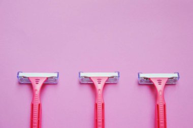 Pembe arka planda birkaç pembe tıraş bıçağı var.