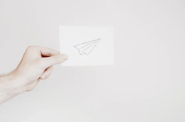 Man holding a paper with drawing of an airplane on white background