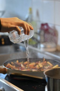 Mutfakta yemek pişirme, tavada sebze kızartma ve su ekleme fotoğrafı.