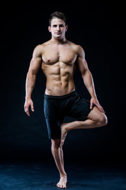 Genç güçlü atlet siyah arka plan üzerine yoga yapıyor