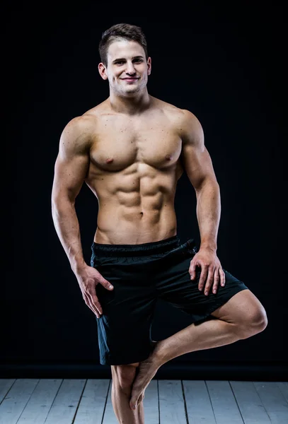 Baalncing Strong atletický muž na jedné noze. Tmavé pozadí. — Stock fotografie