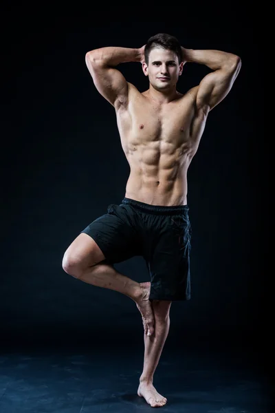 Muskularny mężczyzna balansując na jednej nodze czuje się zrelaksowany ciemnym tle — Zdjęcie stockowe