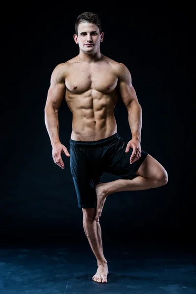 Молодой сильный спортсмен делает йогу на черном фоне — стоковое фото