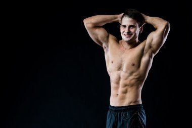 Şortlu gömleksiz adam elleri başının üstünde kameraya bakıyor