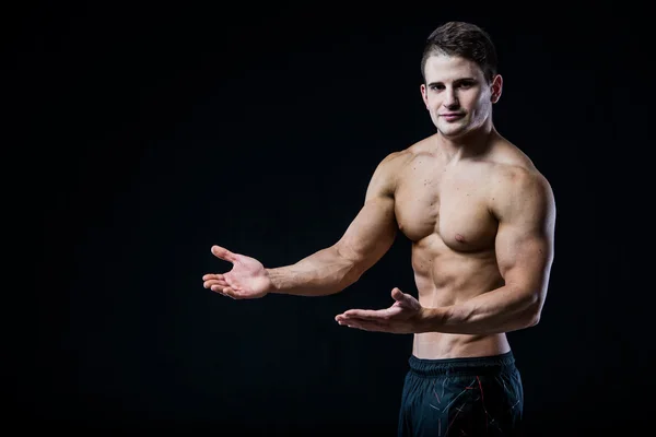 Мускулистый спортсмен указывает двумя руками на пустое копировальное пространство. Сексуальный бодибилдер показывает свое тело на черном изолированном фоновом пространстве . — стоковое фото