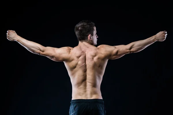 Jeune femme sportive montrant les muscles du dos et des mains sur un fond noir isolé — Photo