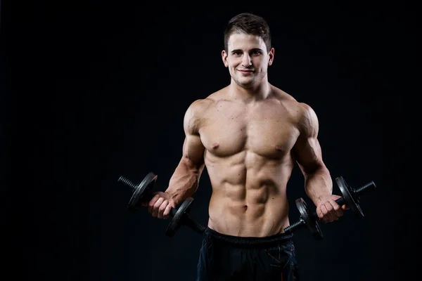 Hombre atlético de poder guapo entrenando bombeando músculos con pesas en un gimnasio. Cuerpo muscular Fitness aislado sobre fondo negro. Mirando a la cámara . — Foto de Stock