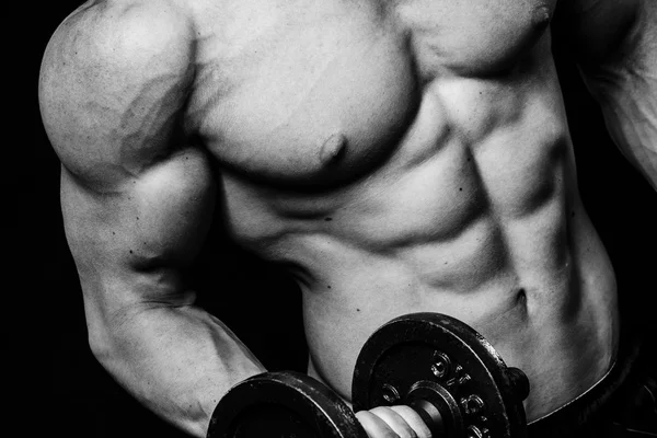 Close up of muscular bodybuilder guy doing exercises with weights dumbbell over isolated black background. Black and white — Stock Photo, Image