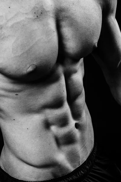 Torso sexy muscular de jovem desportista com abdominais perfeitos de perto. Preto e branco isolado no fundo preto — Fotografia de Stock