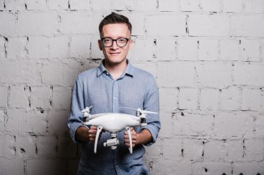 Young stylish Man in glasses holding the quadcopter drone DJI Phantom 4 on a grey brick wall